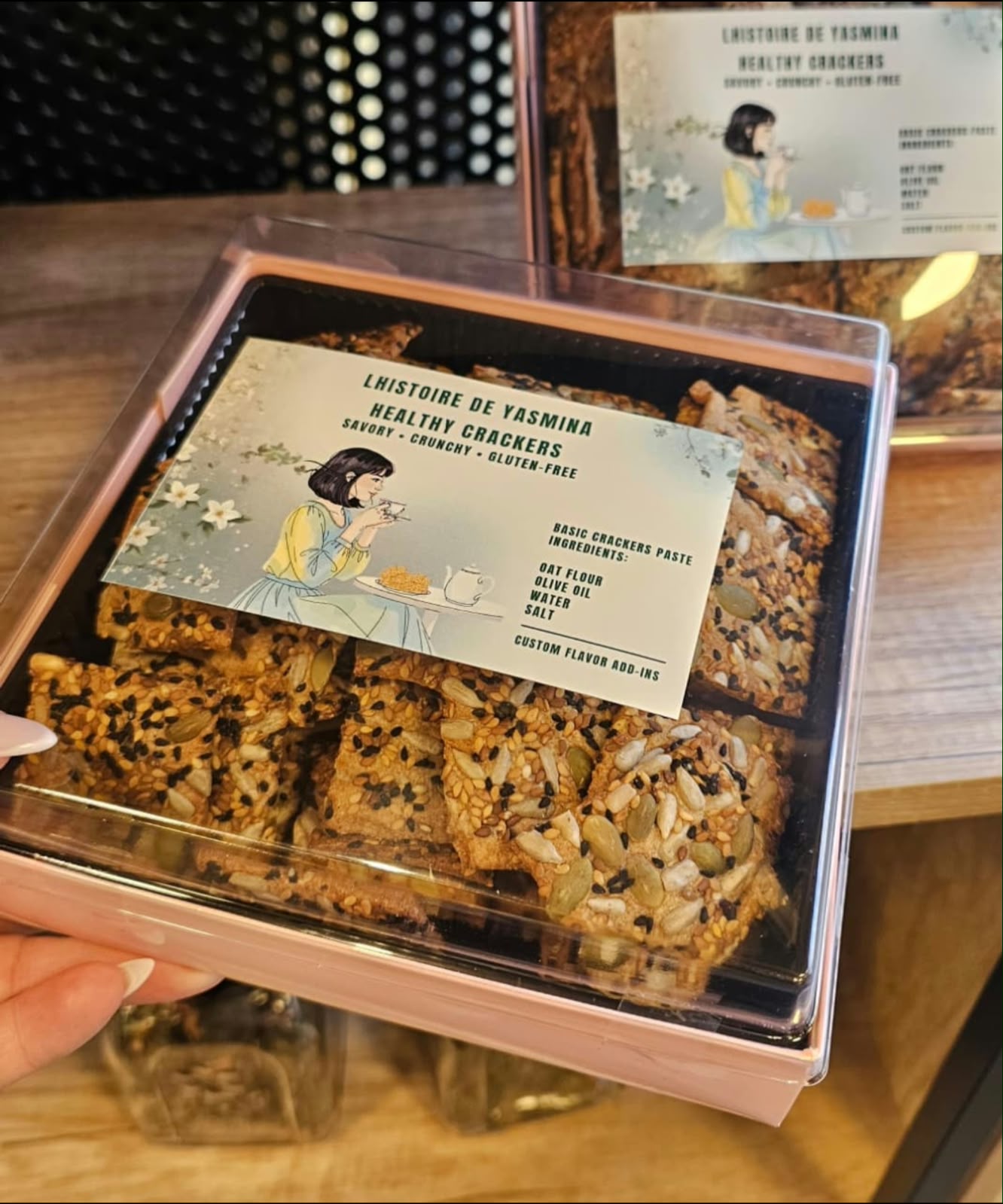 A pink gift box of L'histoire de Yasmina healthy seeded crackers with an illustrated label